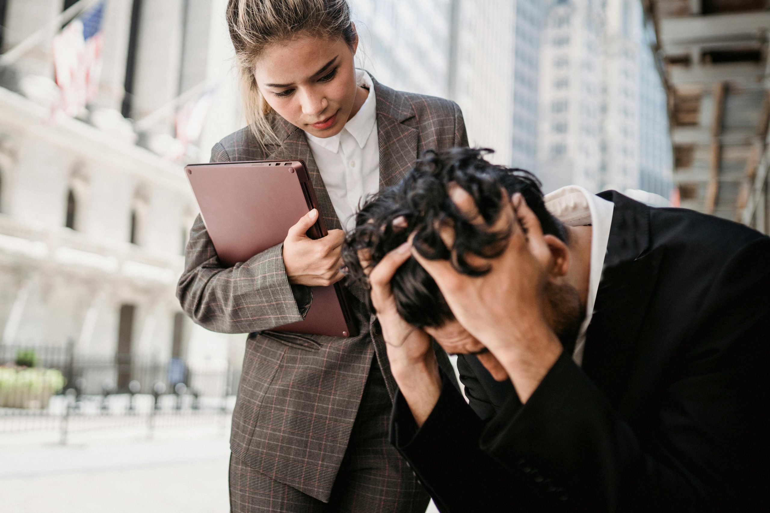 A woman comforts a distressed man in a business environment outdoors.